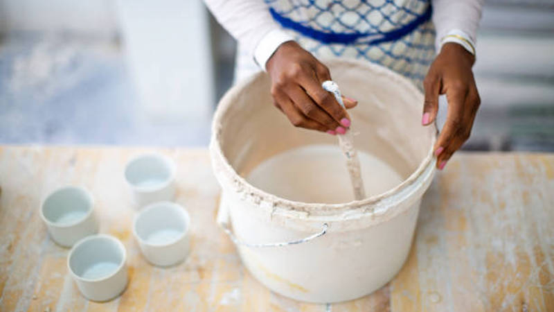 image of a person making pottery slip and mixing with a large wooden spoon
